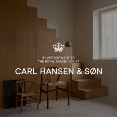 Y-stole placeret nænsomt ved siden af hinanden i et minimalistisk lokale, med et "Carl Hansen & Søn" logo tydeligt placeret i forgrunden af billedet