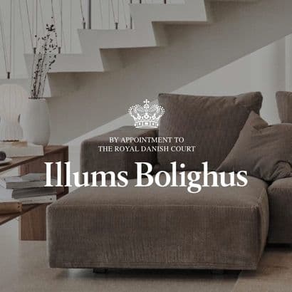 En moderne, møbleret stue med trappe i baggrunden, med et "illums bolighus" logo tydeligt placeret i forgrunden af billedet